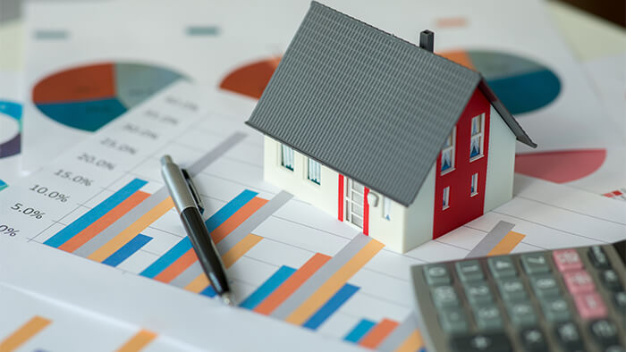 model of a home on top of printed charts and graphs SRS